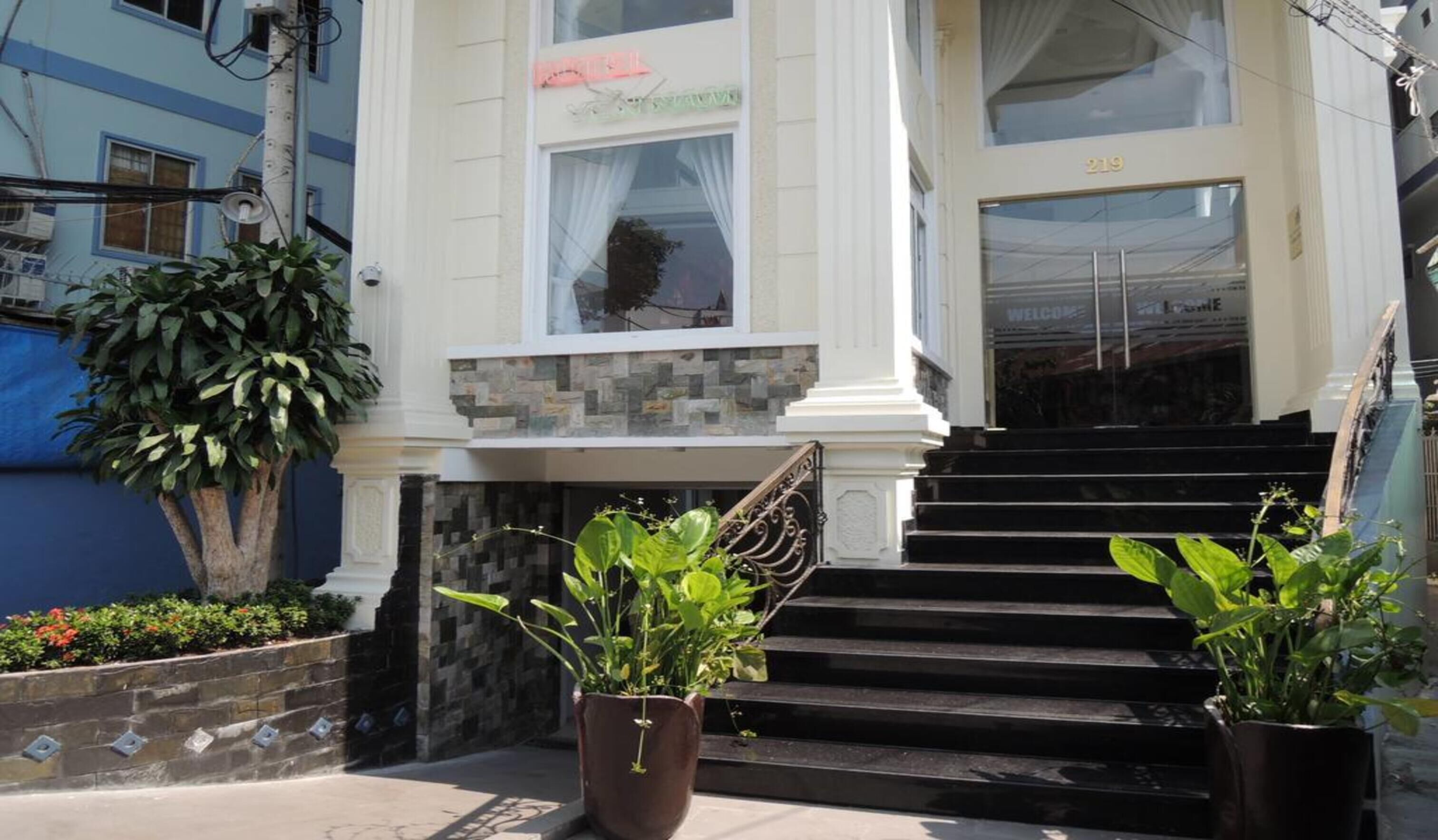 A building with a stone facade, a set of black stairs leading to a door marked "219", and potted plants in front.