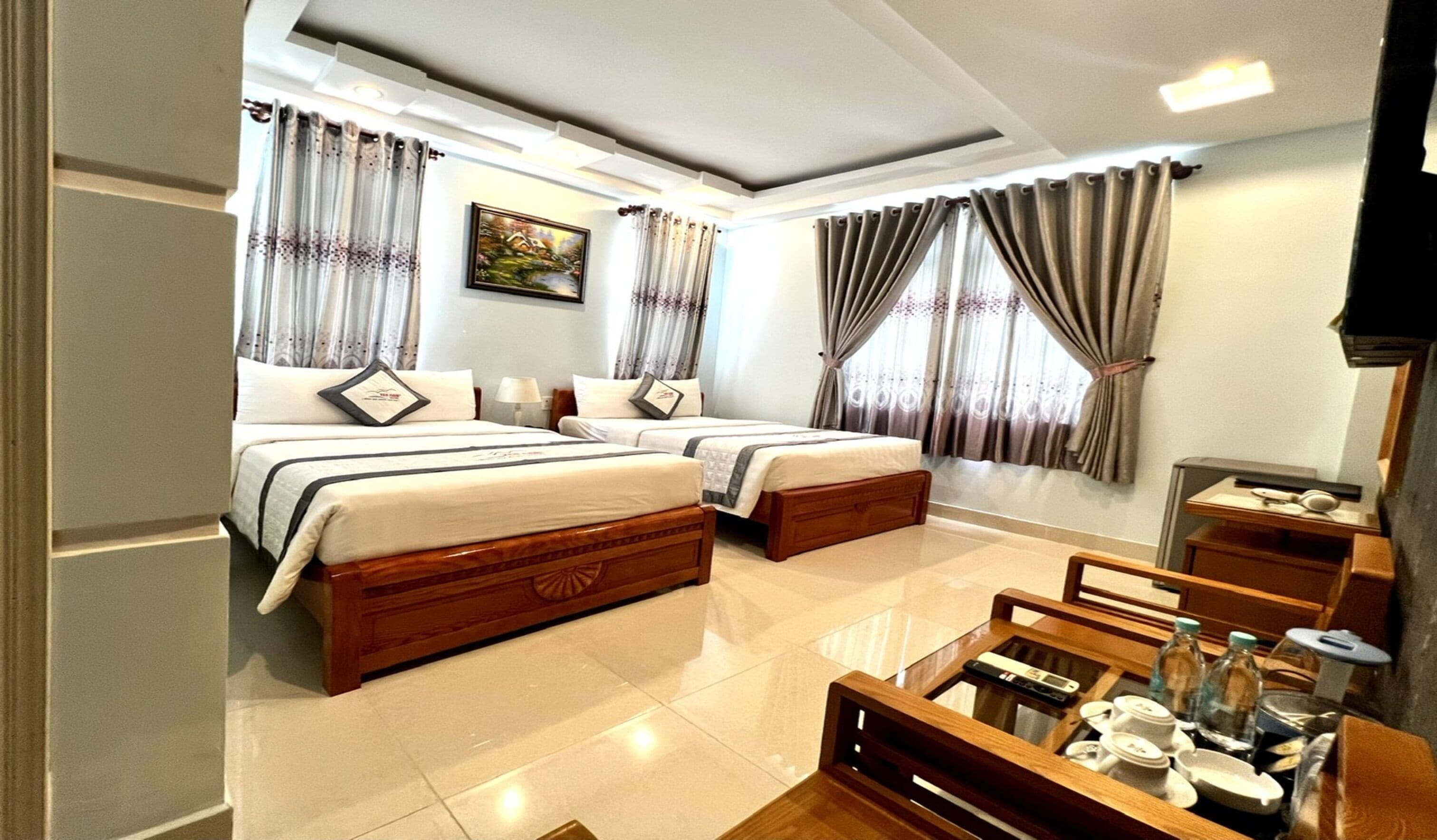 A hotel room with two beds, a wooden coffee table with amenities, and curtains on the windows.