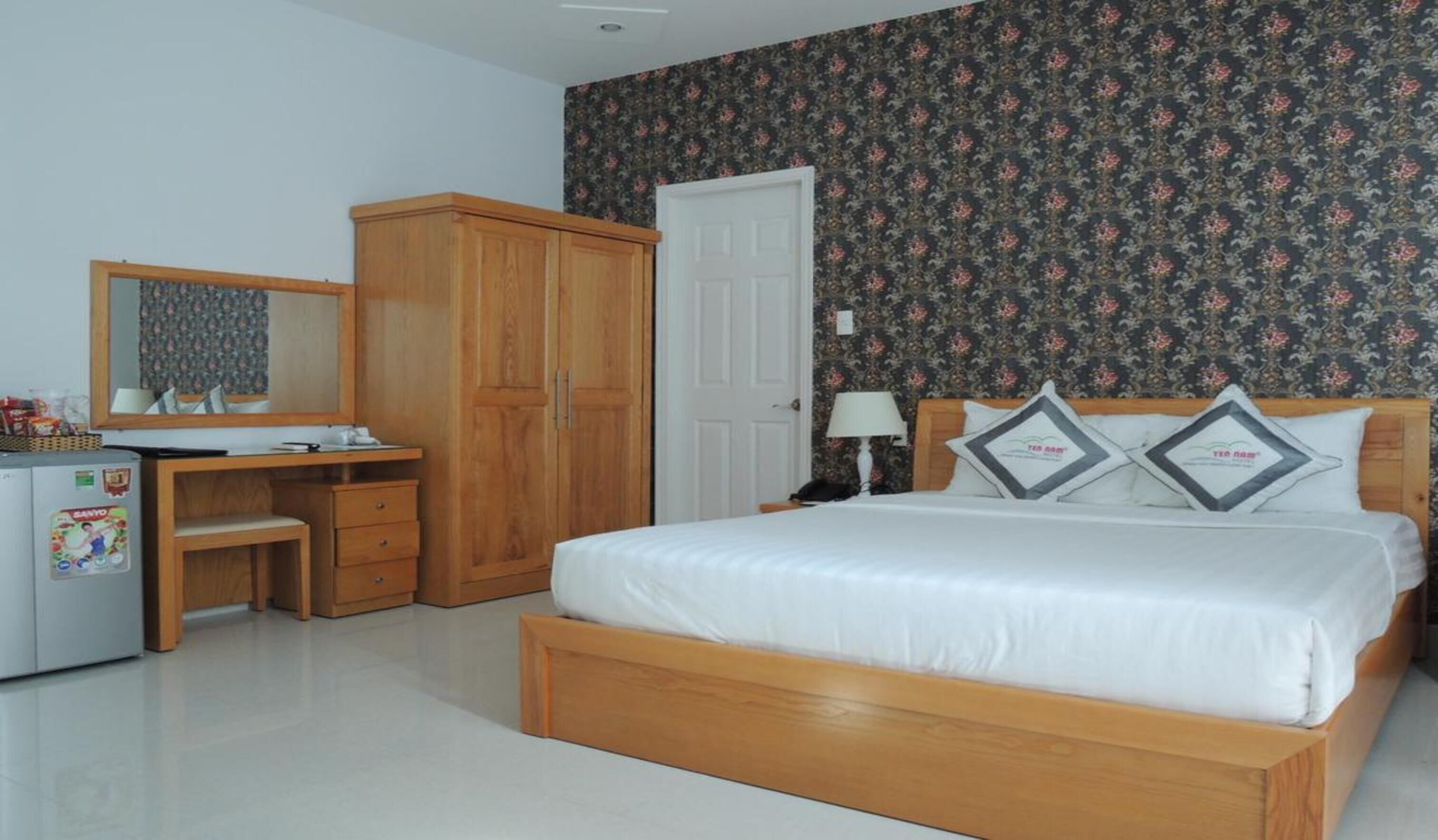 A bedroom with a wooden bed, a desk with a mirror, a wardrobe, and a door.