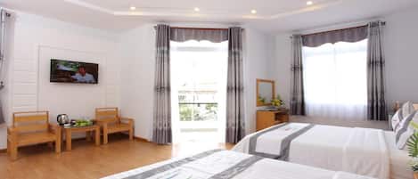 A hotel room with two beds, a desk with a chair, a television, and a balcony with curtains.