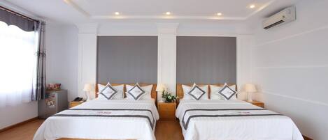 A double room with two beds, a small bedside table with a lamp, and a large window with curtains.
