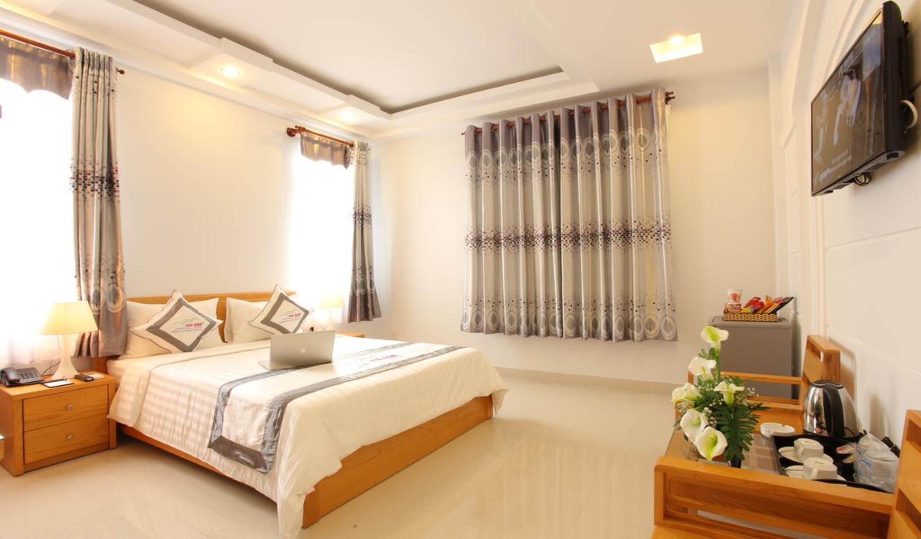Habitación de hotel con cama, escritorio, televisión y ventana con cortinas.