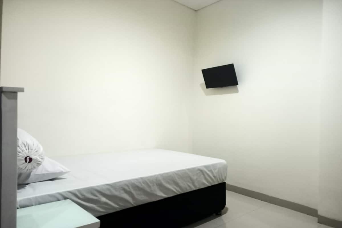 Una habitación pequeña y sencilla con cama, una mesita y televisor montado en la pared.
