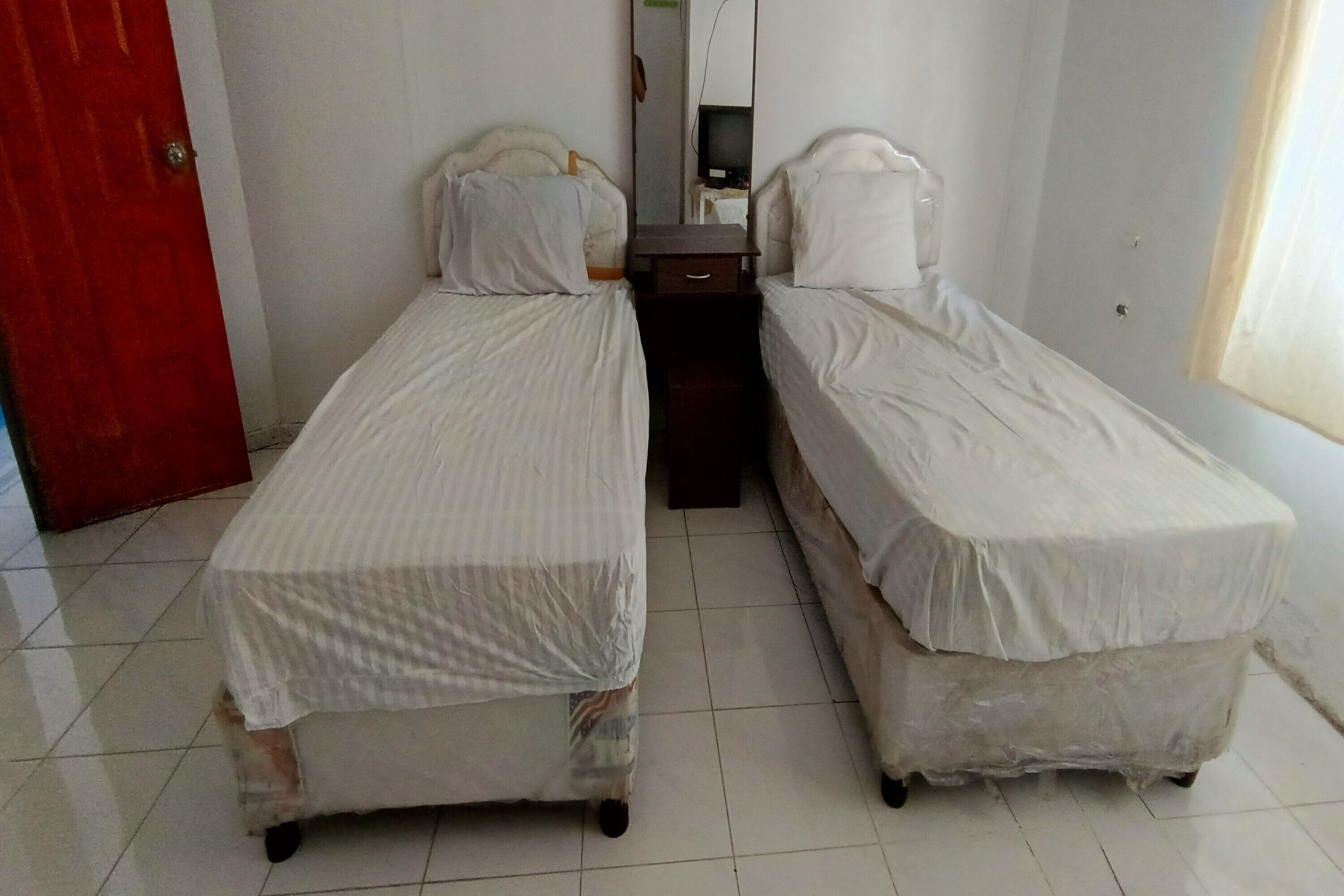Ein kleines Zimmer mit zwei Einzelbetten, einer roten Tür und einem Spiegel an der Wand.