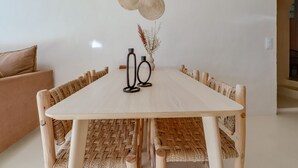 Ein Essbereich mit einem hellen Holztisch, Korbstühlen und einer Vase mit getrockneten Pflanzen.