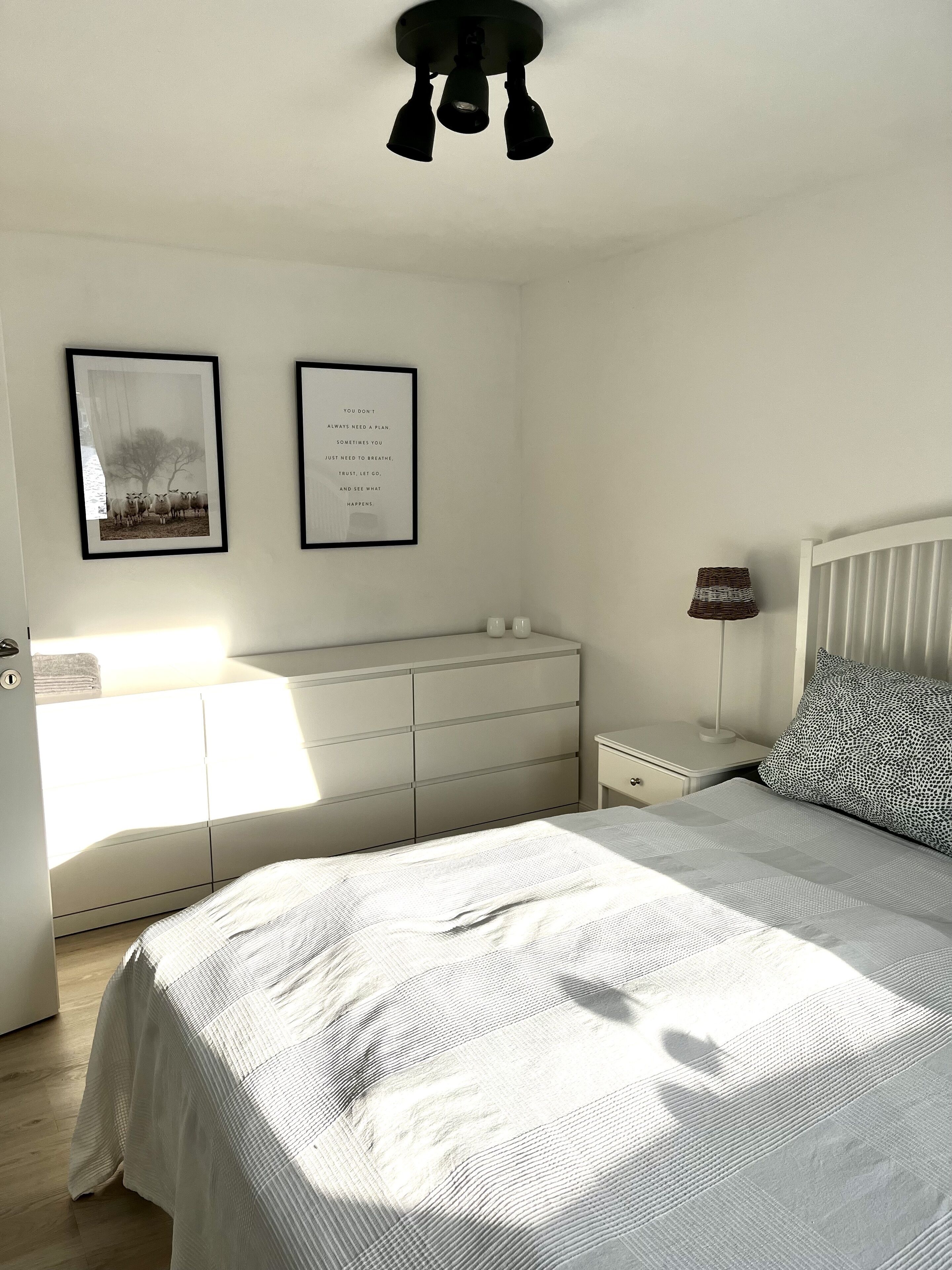 A bedroom with a bed, dresser, nightstand, lamp, and two framed pictures on the wall.