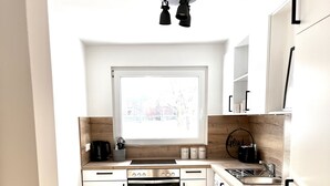 Una cocina moderna con armarios blancos, horno empotrado, placa de cocción y ventana sobre el fregadero.