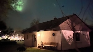 Una casa con porche y banco, bajo un cielo nocturno lleno de estrellas.
