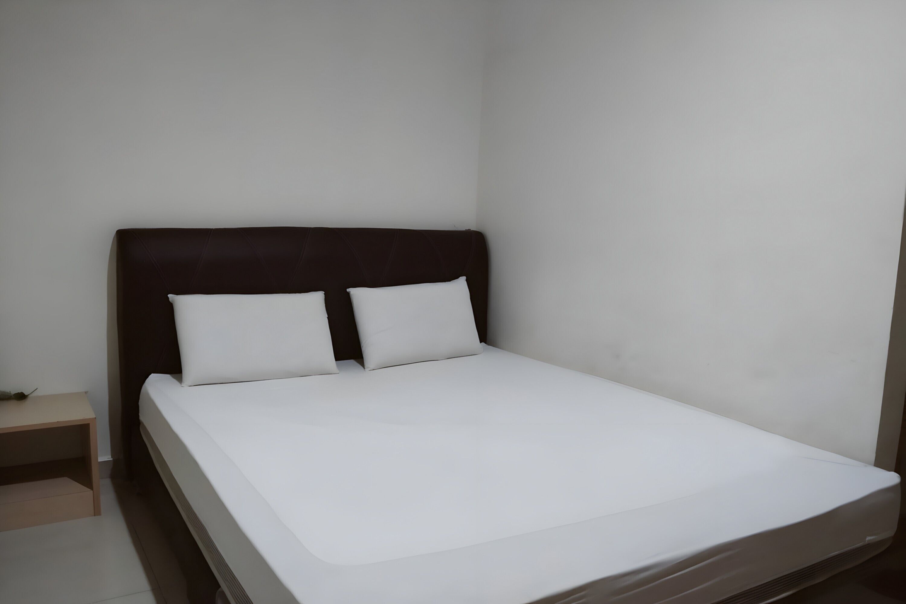 A single bed with a dark headboard and white bedding in a room with plain white walls.