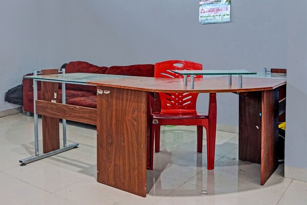 A room with a wooden bed, a glass-top table, a red chair, and a wall-mounted calendar.
