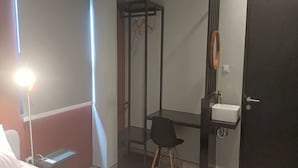 Une chambre d’hôtel comprenant un lit, un bureau avec une chaise, une petite table, une armoire, un porte-manteau et un lavabo.