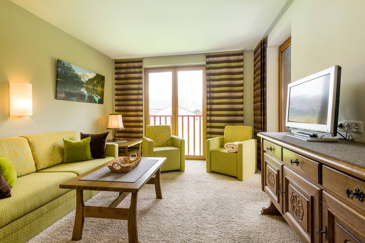 A living room with a sofa, two armchairs, a coffee table, a television, and a large window with curtains.