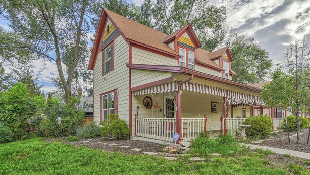 Ein zweistöckiges Haus mit Veranda, umgeben von einem gepflegten Garten und Bäumen.