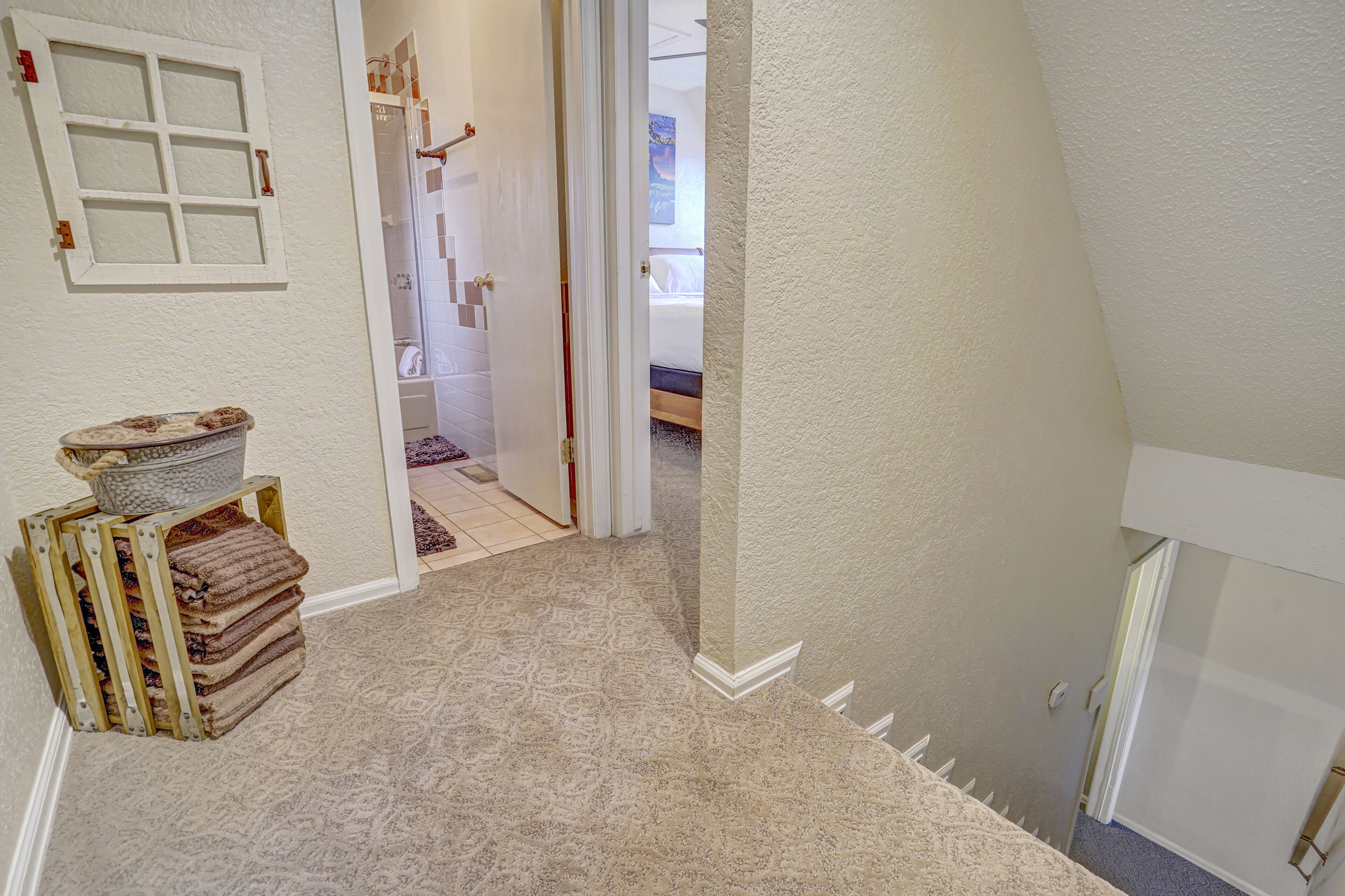 A hallway with a carpeted floor, a wooden bench with towels, and a door leading to a bedroom.