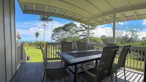 Een overdekt buitengebied met een tafel en stoelen, een uitzicht op de oceaan en een gazon.