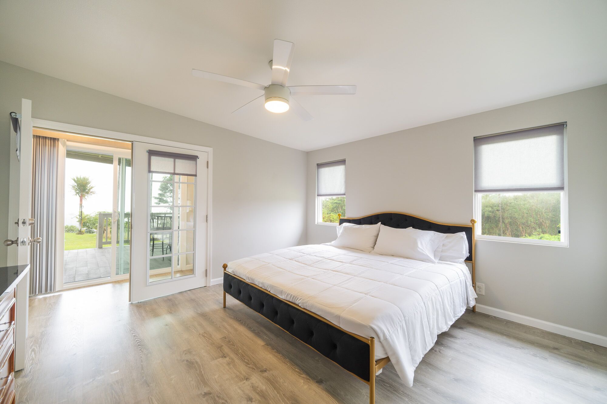 Une chambre à coucher avec un lit, un ventilateur de plafond et une porte-fenêtre coulissante donnant sur un balcon.