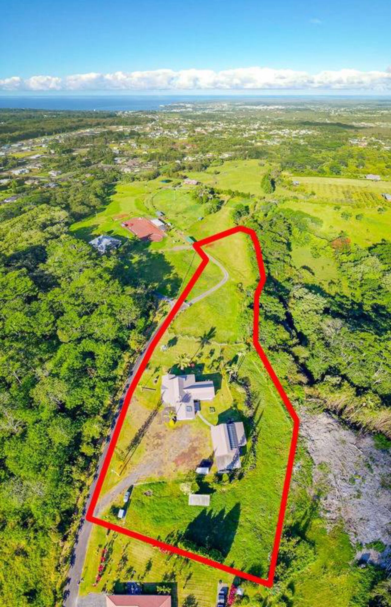 An aerial view of a property with a large green field, a small building, and a winding road.