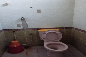 A small bathroom with a toilet, a red bucket, and a visible water leak on the wall.