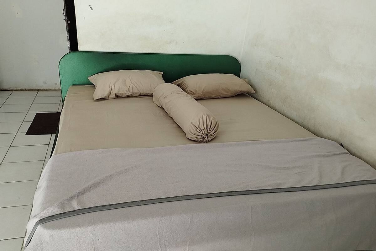 Una cama individual con cabecera verde y dos almohadas color beige.
