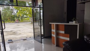 A reception area with a glass door leading outside, a reception desk, and a black leather couch. - Hotel O Losmen Karunia Katingan Near Kantor Sekretariat PPK Katingan Kuala (Pegatan Hilir)
