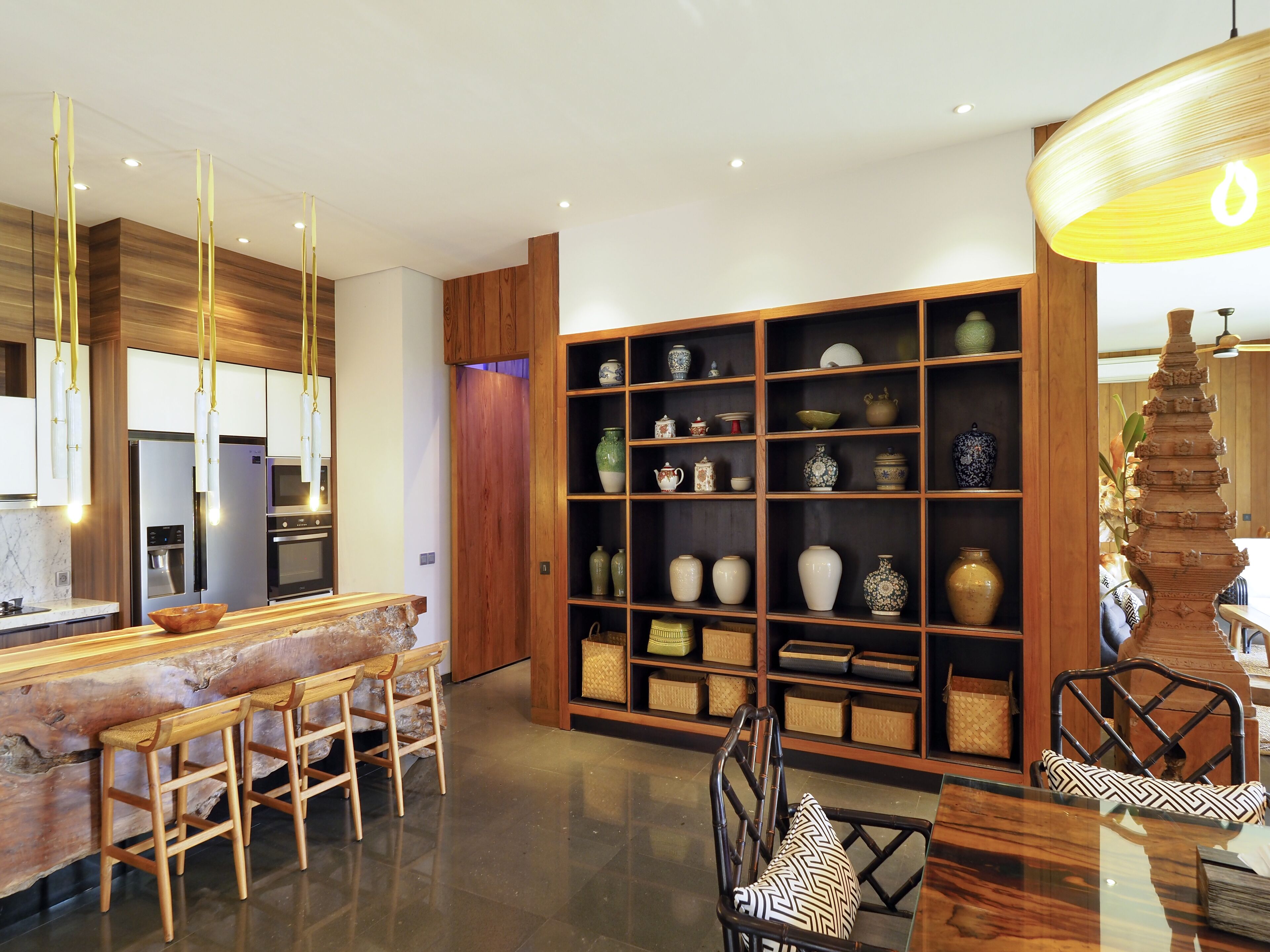 Een moderne keuken met roestvrijstalen apparatuur, houten barkrukken en een decoratieve plank met diverse aardewerkobjecten.