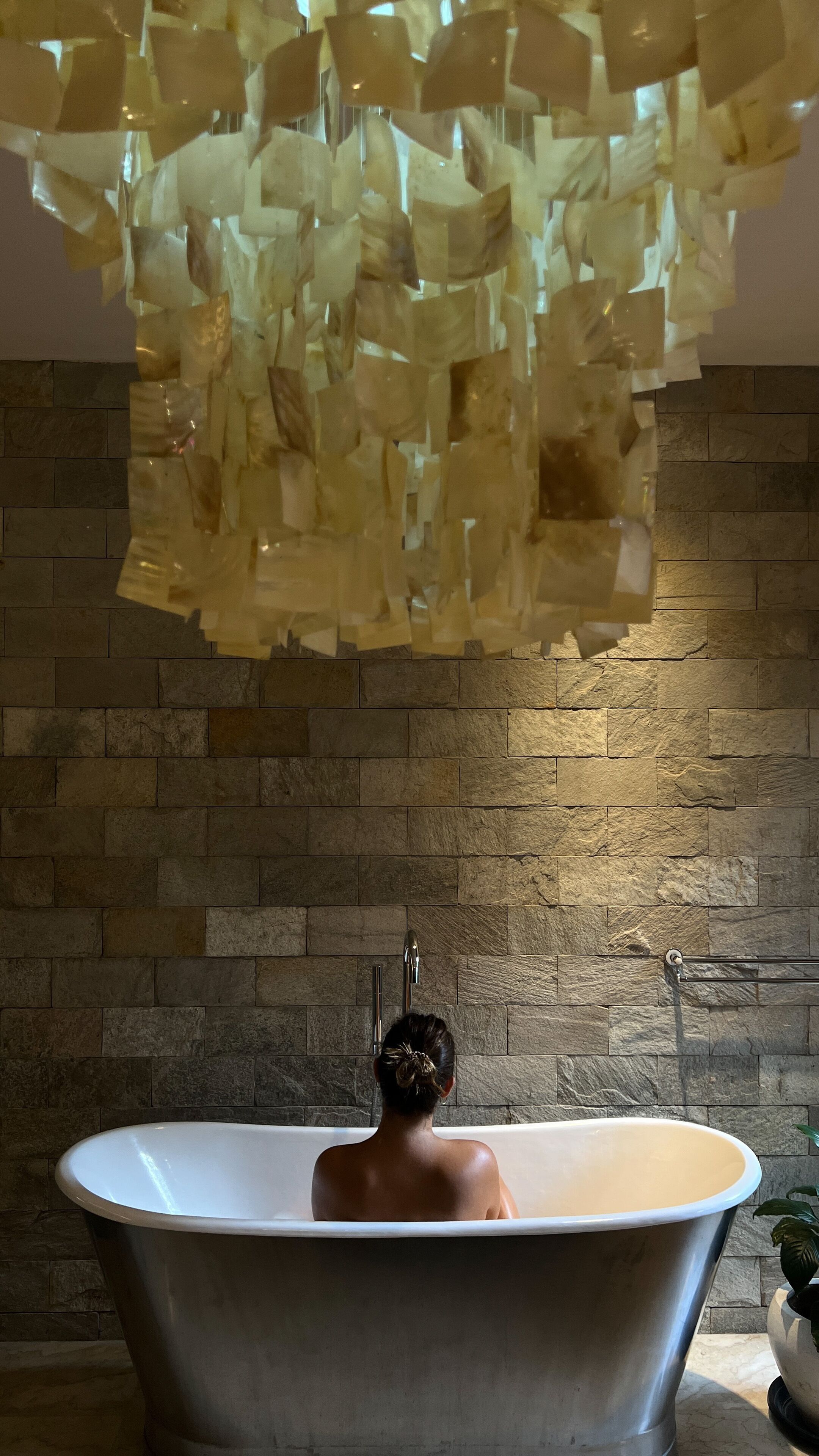Une personne assise dans une baignoire, avec un mur de pierre en arrière-plan.