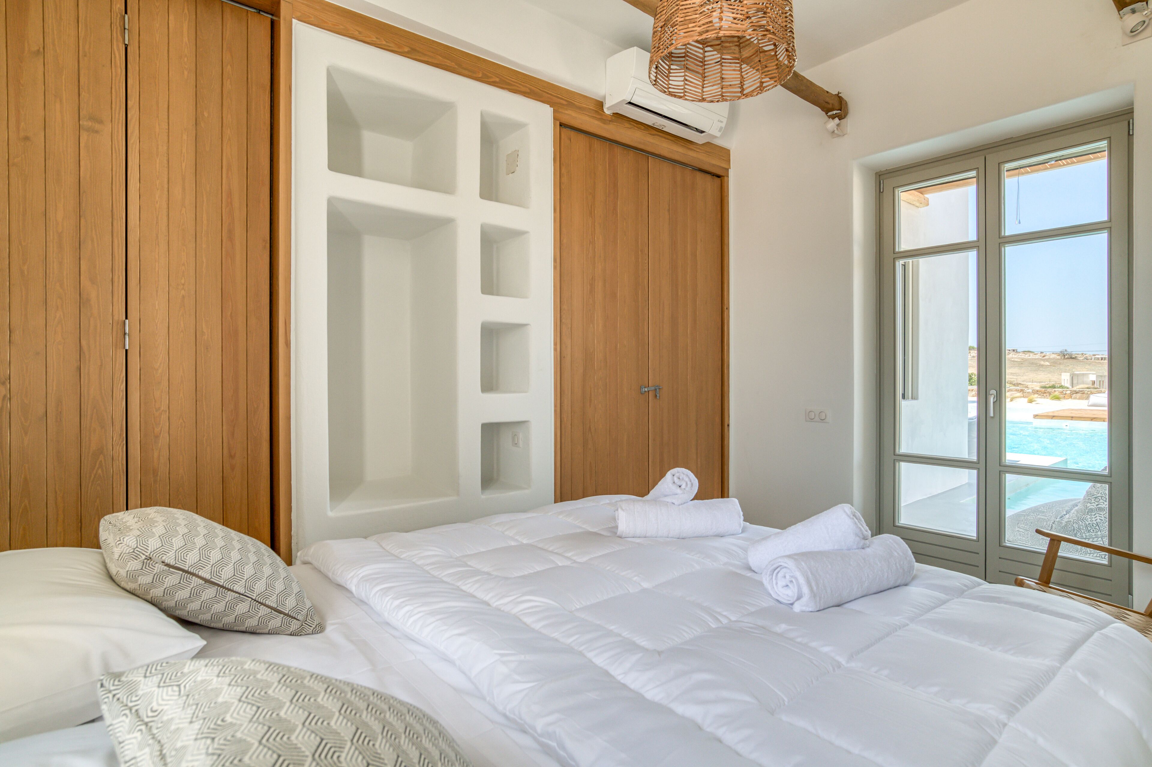 A bedroom with a large bed, a wooden wardrobe, and a window with a view of the sea.
