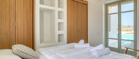 A bedroom with a large bed, a wooden wardrobe, and a window with a view of the sea.