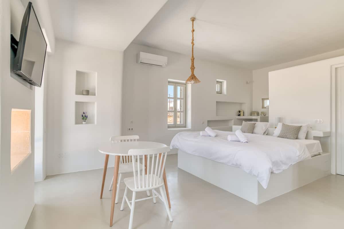 A modern bedroom with a large bed, a dining table, and a TV mounted on the wall.
