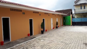 A building with multiple doorways, some with potted plants, and a tiled courtyard. - OYO 93518 Kepayang Guesthouse Syariah (Bandar Lampung)