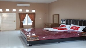 A bedroom with a large bed, a dresser, a mirror, and a door. - OYO 93518 Kepayang Guesthouse Syariah (Bandar Lampung)