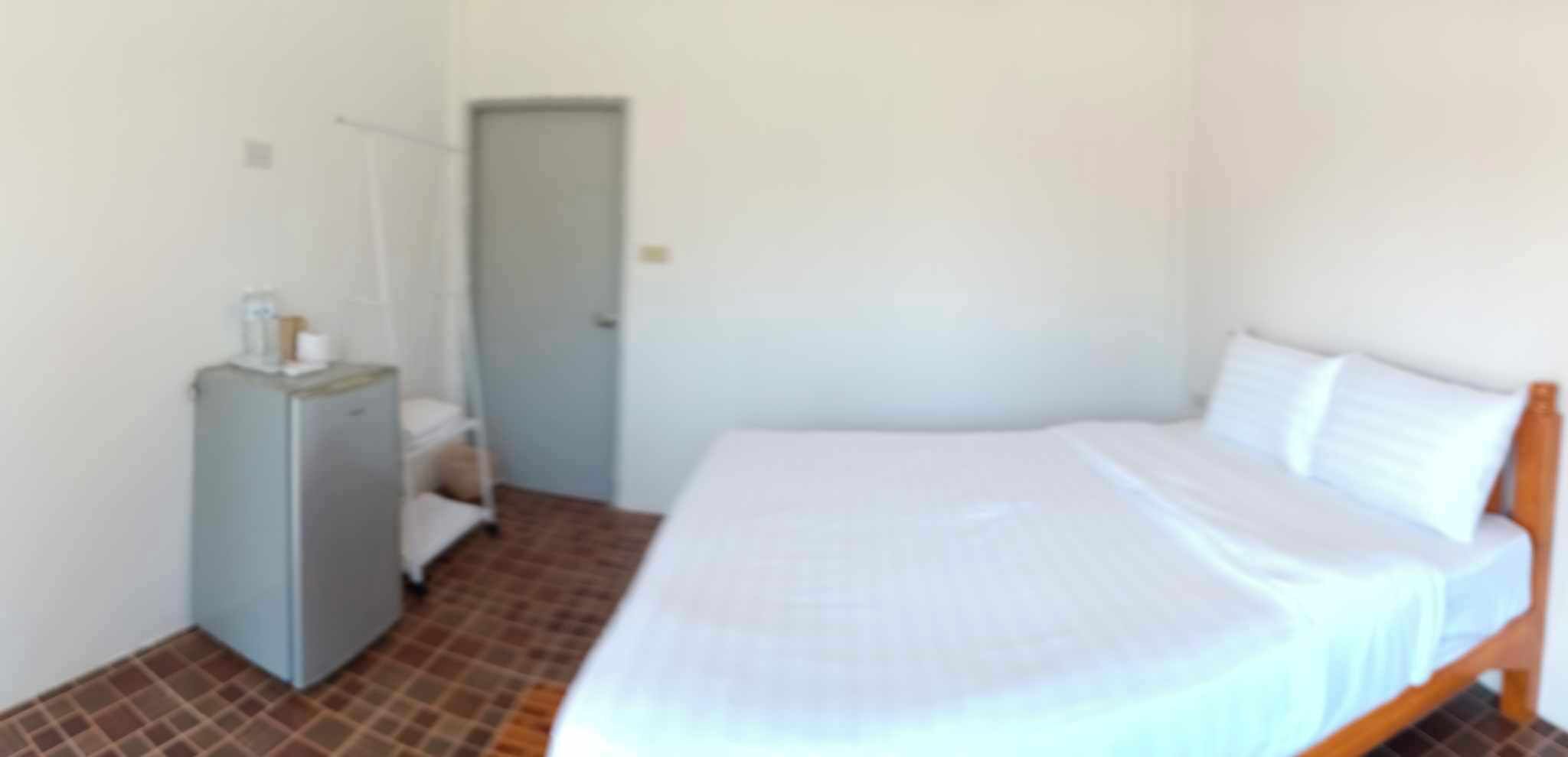 A small, single-bed room with a wooden headboard, a small desk with a chair, and a door leading to another room.