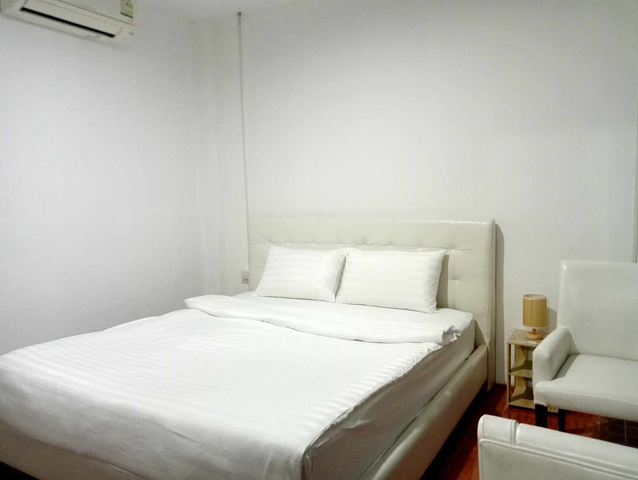 Een net opgemaakt bed met witte lakens in een eenvoudige kamer met witte wanden en een klein nachtkastje met een lamp.