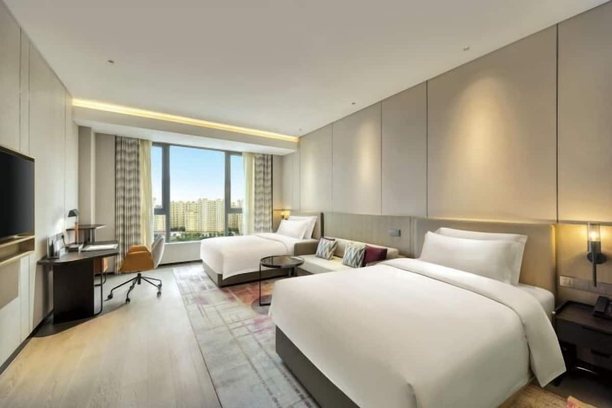 Une chambre d’hôtel avec deux lits, un bureau, une chaise, une télévision et une grande fenêtre donnant sur la ville.
