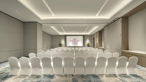 Una sala conferenze con file di sedie bianche, un grande schermo fronteggiante la stanza e un design moderno del soffitto.