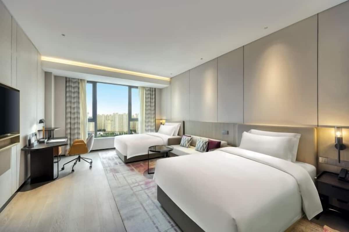 Une chambre d’hôtel avec deux lits, un bureau, une chaise, une télévision et une grande fenêtre donnant sur la ville.