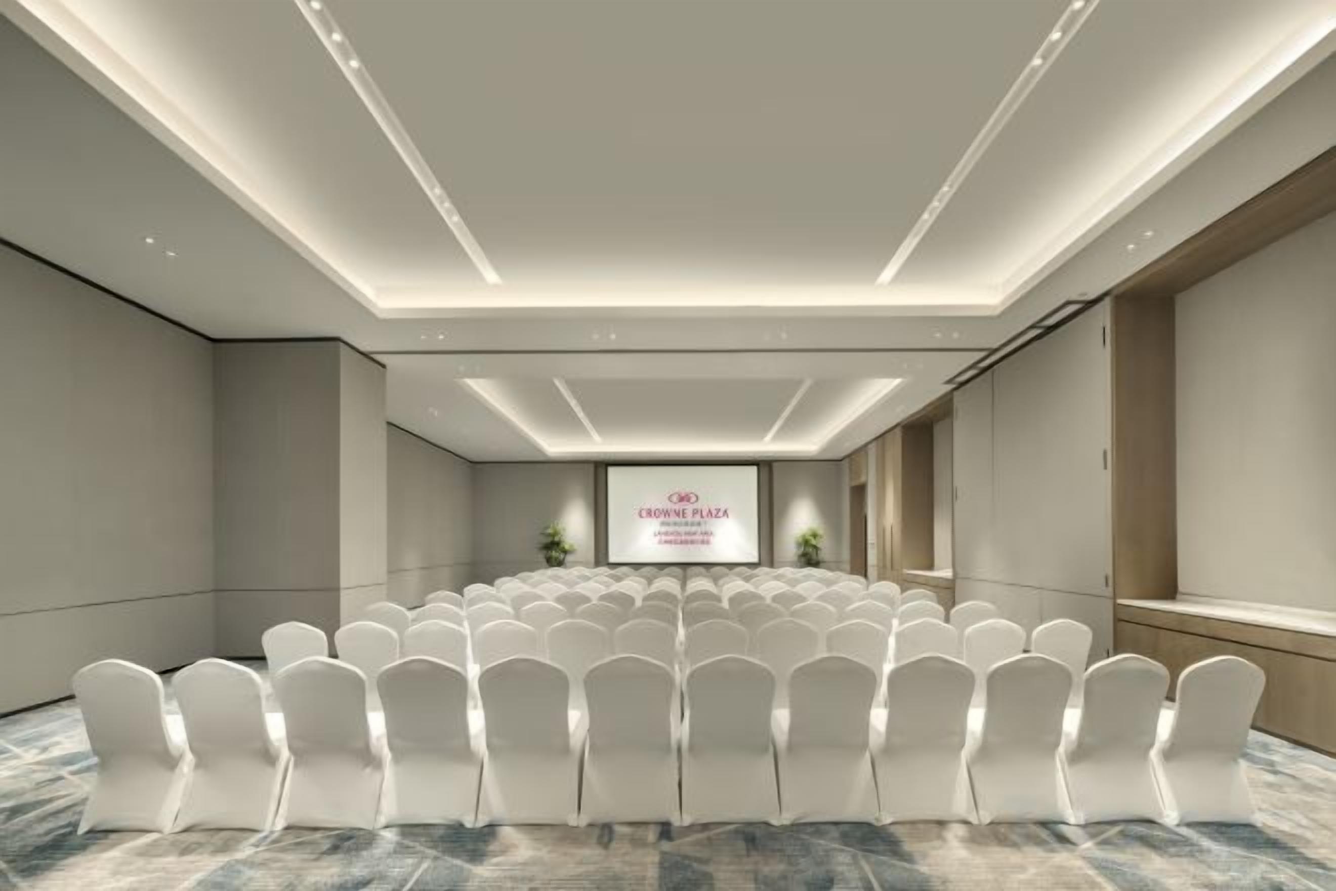 A conference room with rows of white chairs, a podium, and a large screen displaying text.
