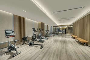 Une salle de sport moderne équipée de machines de cardio, de bancs et d’un mur recouvert de miroirs.