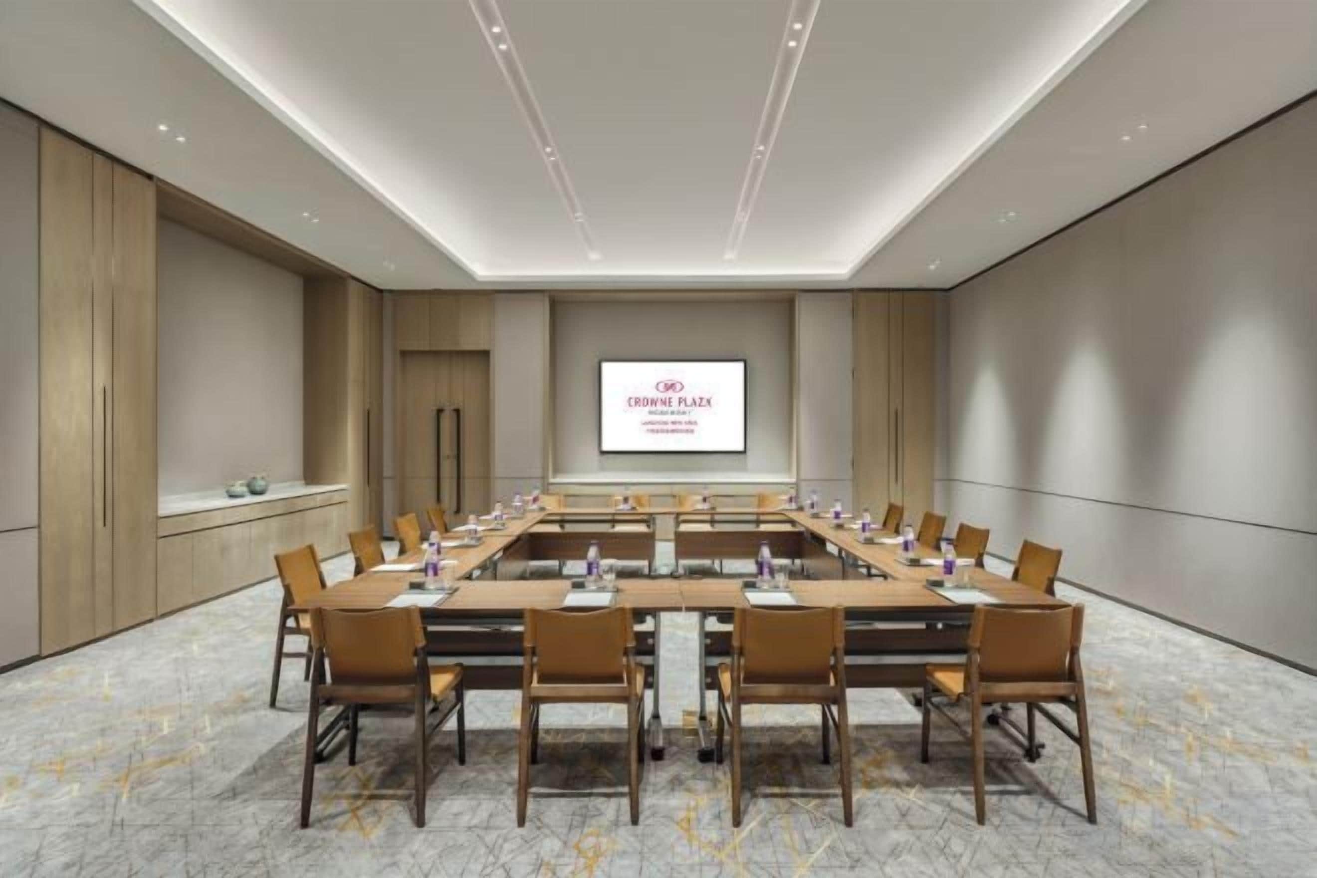A conference room with a long table, chairs, a projector screen, and a marble floor.
