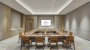 A conference room with a long table, chairs, a projector screen, and a marble floor.