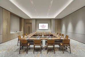 Un salón de conferencias con una larga mesa, sillas, una pantalla de proyector y piso de mármol.