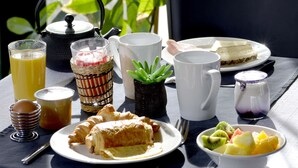 A breakfast table with a croissant, fruit bowl, tea, and a teapot.