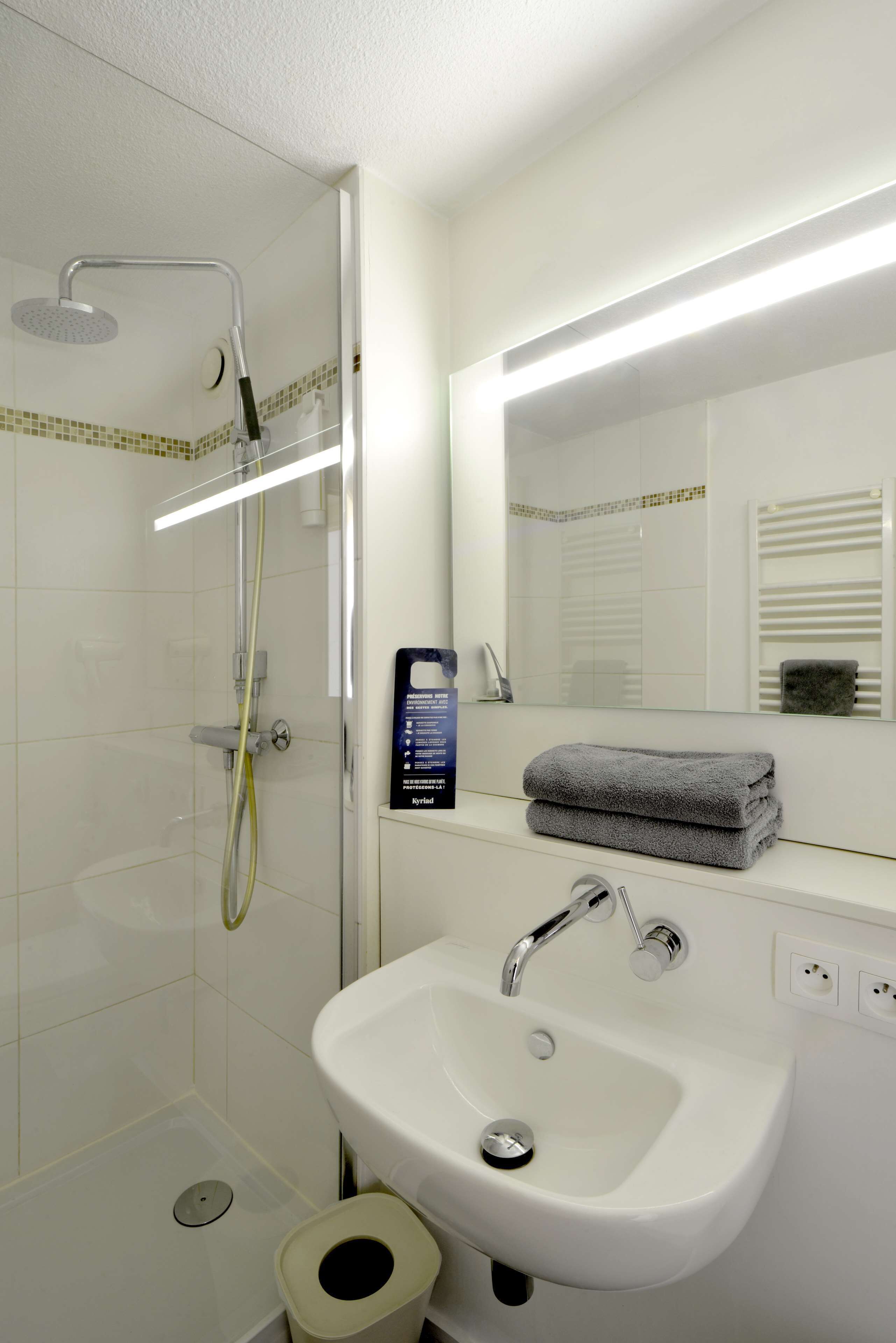 Un baño moderno con ducha de vidrio, un lavamanos blanco y un espejo encima.