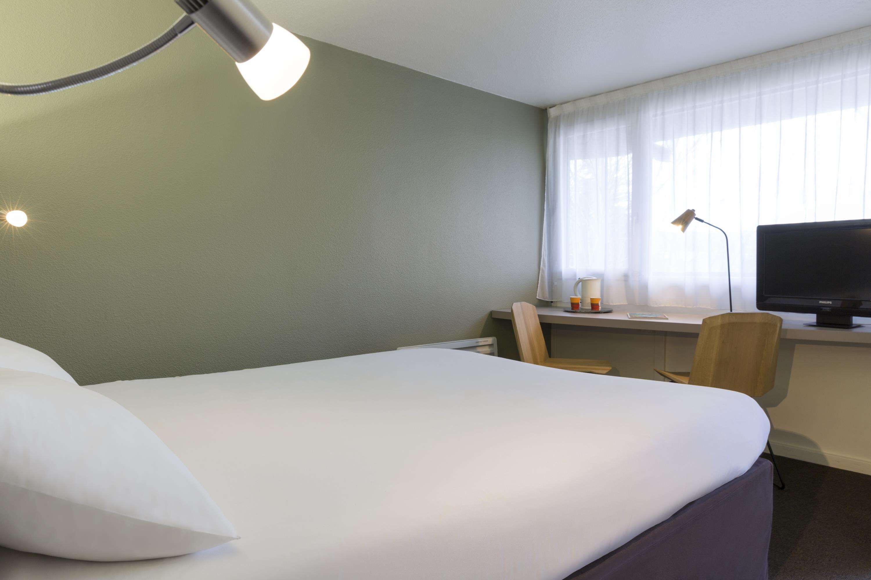 Una habitación de hotel con cama, escritorio con silla, televisor y ventana con cortinas.