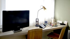 A desk with a computer monitor, a lamp, a coffee maker, and a tablet.