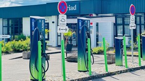 A charging station area with electric vehicle charging points, a building with a blue roof, and directional signs.