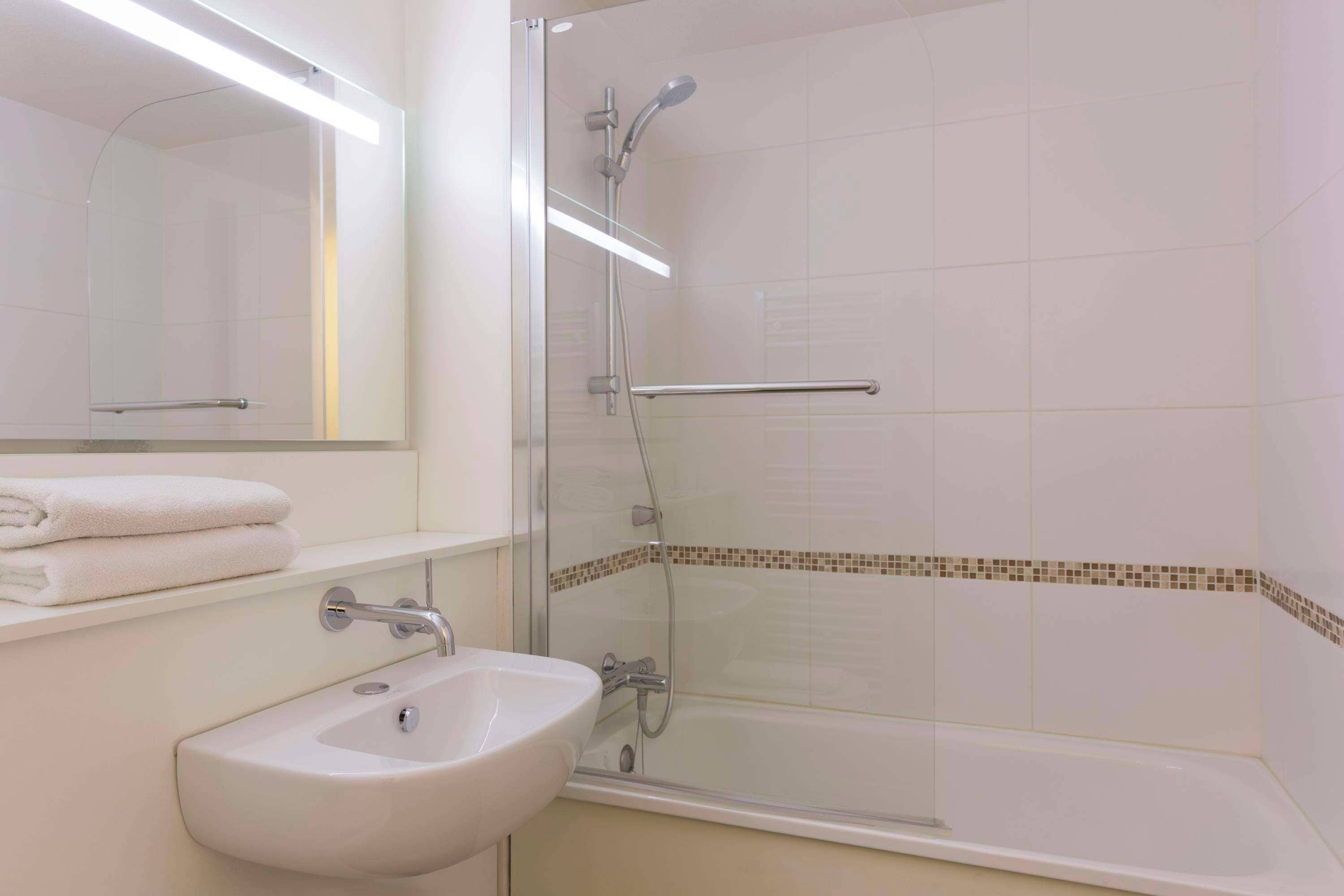 A bathroom with a sink, mirror, and shower.