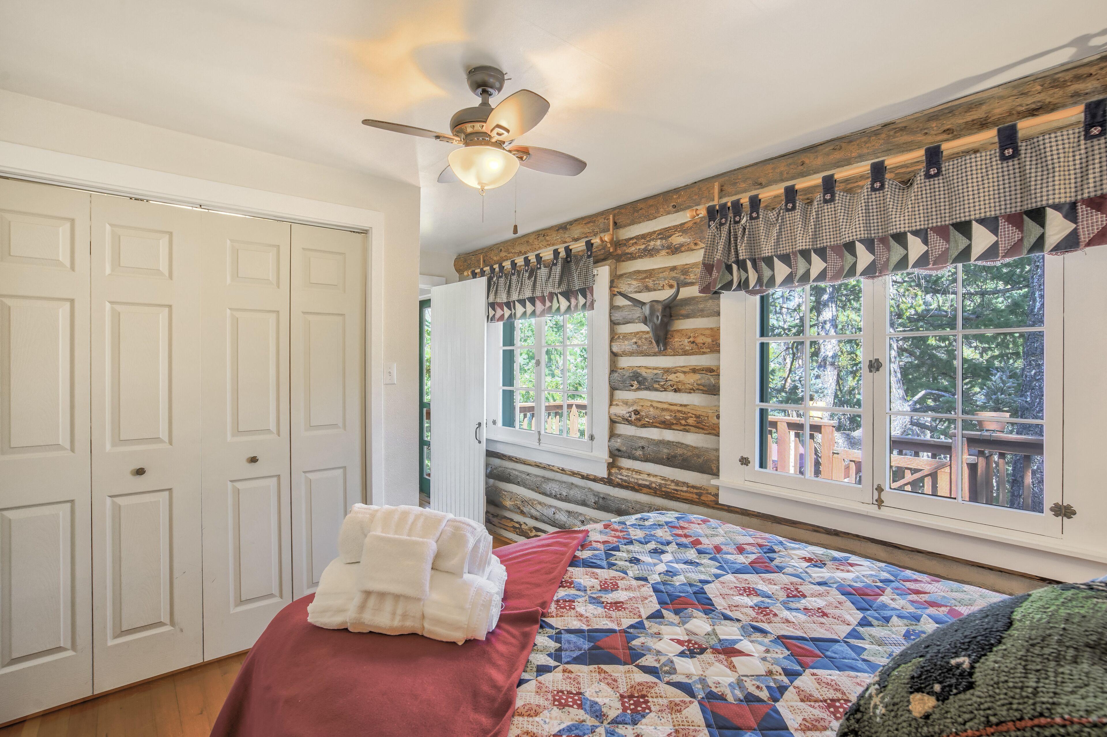 A bedroom with a bed, a ceiling fan, a window with curtains, and a view of the outdoors.