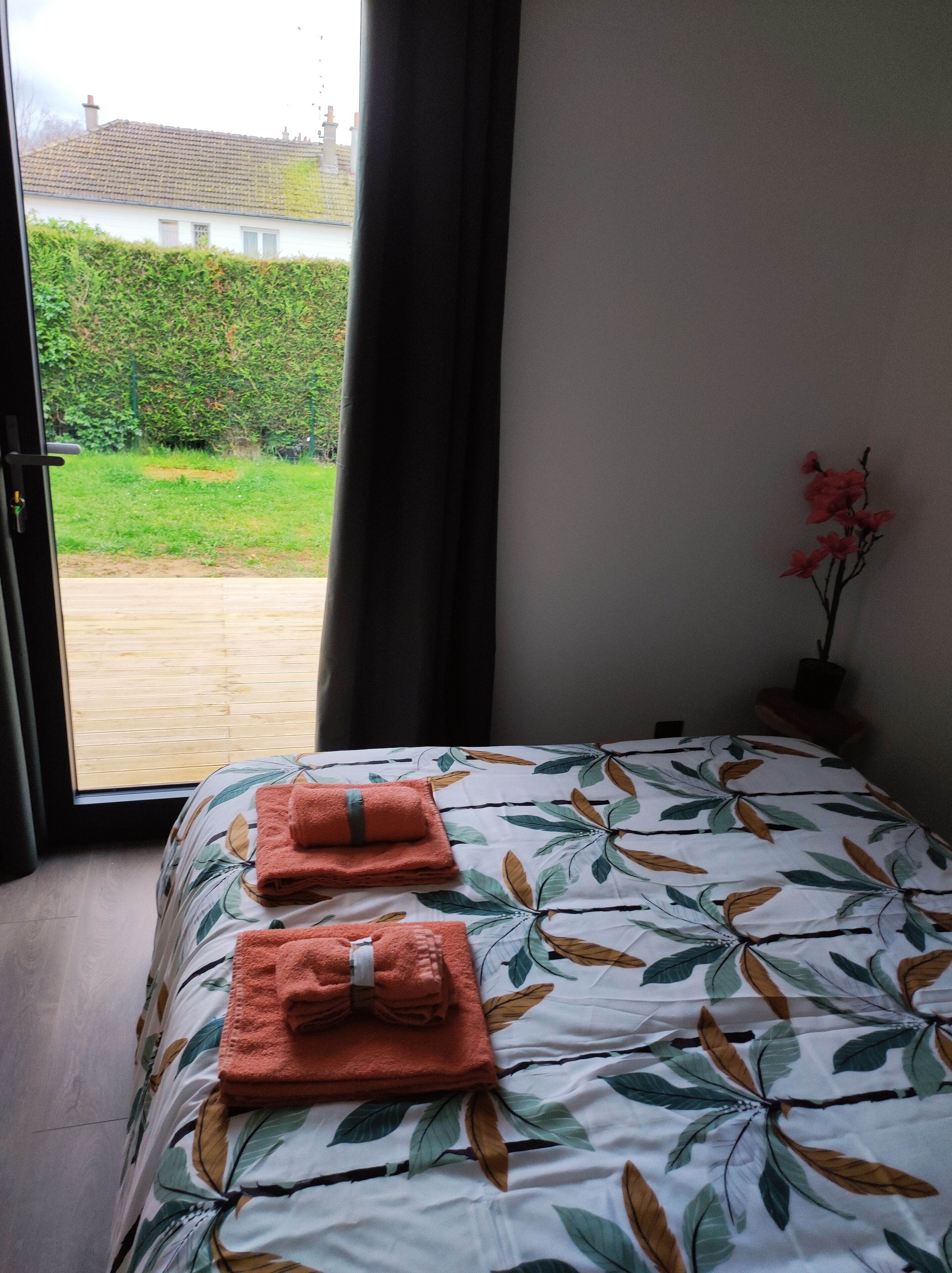 A bedroom with a bed, two towels, a window, and a view of a garden.