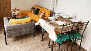 Uma área de refeições com uma mesa posta para dois, um sofá com almofadas laranjas e um abajur na parede.